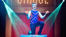 Actor in CIRQUE - The Greatest Show knelt on one knee and holding juggling balls in both hands as he sings
