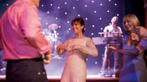 A woman in a pink dress dancing with others at a lively event.