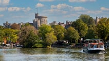 A view of Windsor Castle from the River Thames, featuring a boat in the foreground and surrounded by greenery