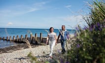 A man and woman stroll together along a serene beach, enjoying the sun and waves.