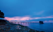 A serene pier at dusk, framed by a blue sky adorned with soft clouds, creating a tranquil evening atmosphere.