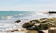 Ocean waves crashing against a rocky beach under a clear blue sky.