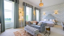 Spacious manor house bedroom at Heythrop Park featuring a bed, chair, lamp, and a large window for natural light.