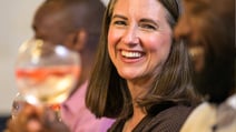 A cheerful woman holds a glass of wine, smiling at the cocktail tasting event at Heythrop Park.