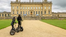 Two riders on segways near the majestic Heythrop Park building, highlighting a unique way to explore the surroundings.