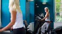 Two people in the gym at Holme Lacy House, smiling at each other as they work out