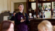 A friendly team member bringing a hot drink to a guest at Holme Lacy House