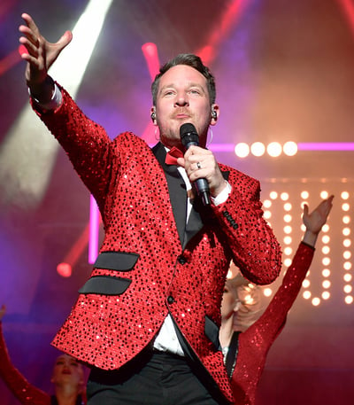 Singer in red suit and black bow tie performing Cirque: The Greatest Show on stage at Warner Hotels.