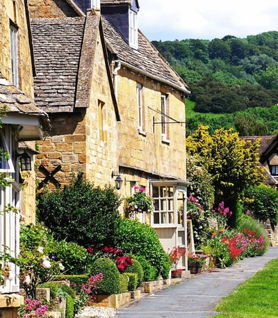 Charming Cotswolds village street with stone houses and colorful flowers.