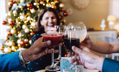 A group of people joyfully toasting with wine glasses in front of a beautifully decorated Christmas tree.