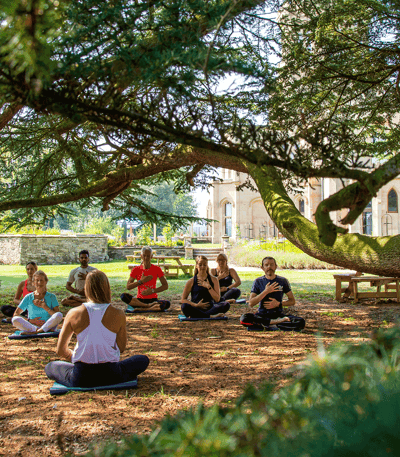 Group of individuals sitting in a circle outdoors, participating in a meditation during a wellness retreat at Warner Hotels.
