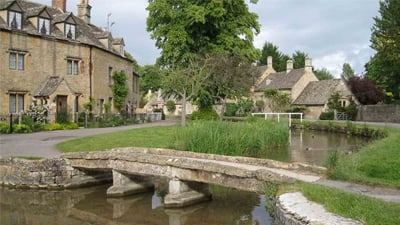 A charming stone bridge crosses a river in Bourton-on-the-Water, a scenic village in the Cotswolds, West Midlands.