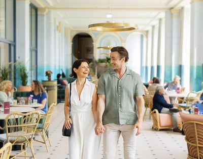 A couple strolls through the elegant lobby of Warner Hotels, surrounded by stylish decor and warm lighting.