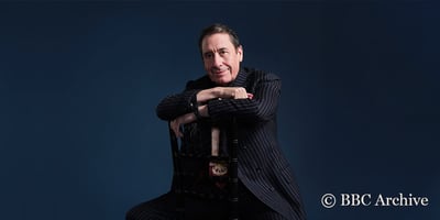 Jools Holland sat backwards on a chair with a coy smile