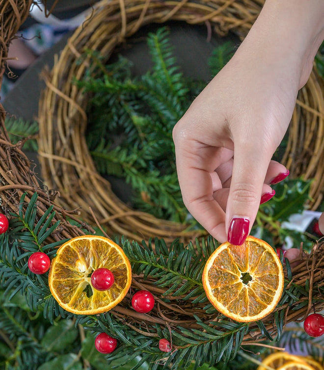 A person making a Christmas wreath, showing a close up of her hand with festive red nails and holding an orange