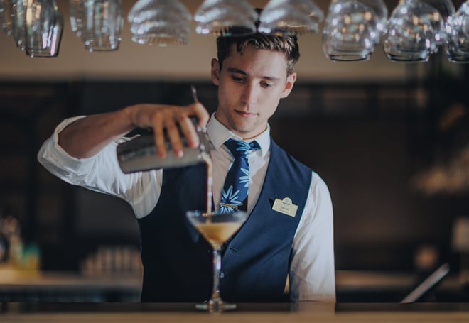 A bartender pours a cocktail from a shaker