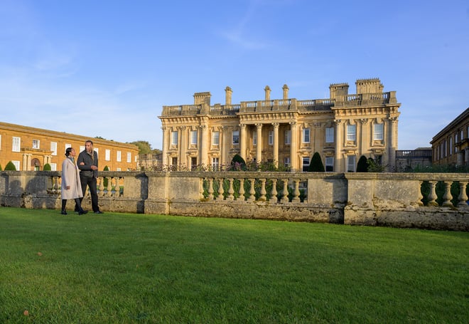 The facade of Heythrop Park with two guests wandering in front of the building