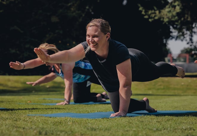 A guest smiling as she performs a yoga pose during a wellness retreat workshop at Heythrop Park