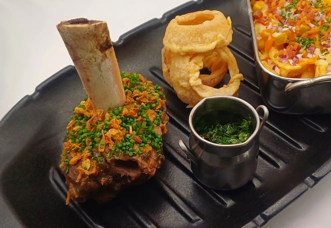 Slow braised beef on the bone: Melt-in-the-mouth tender beef served alongside loaded fries, topped with cheese, bacon, and crispy onions, plus beer-battered onion rings, and a zingy chimichurri sauce.