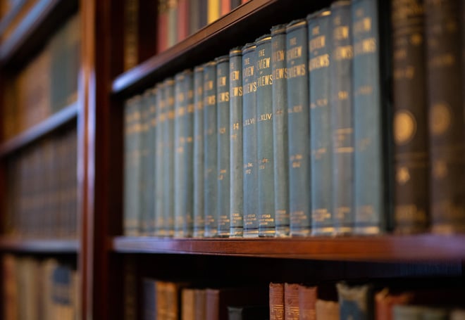 A close-up of neatly arranged blue hardcover books on a wooden shelf, showcasing their spines with gold lettering.