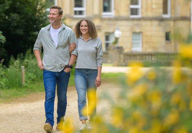 Discover the tranquility of Heythrop Park Hotel as a man and woman enjoy a leisurely walk in the park.