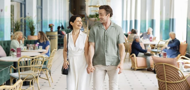 A couple strolls through the elegant lobby of Warner Hotels, surrounded by stylish decor and warm lighting.