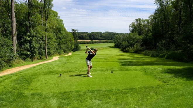 A golfer takes a swing on a vibrant green course, showcasing skill and concentration amidst a sunny backdrop.