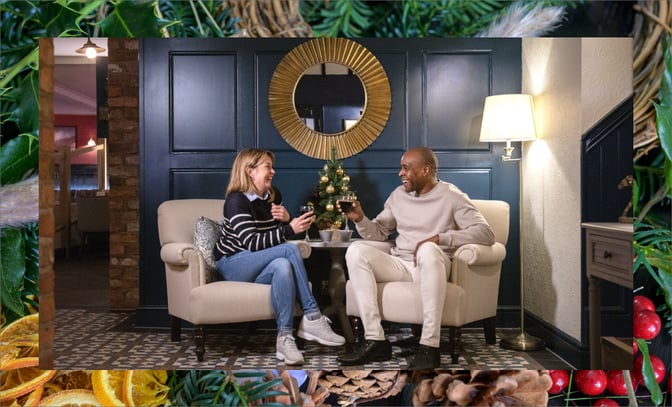 A man and woman relax in chairs, enjoying the festive atmosphere created by a sparkling Christmas tree nearby.