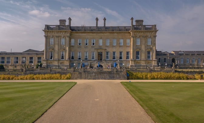 The impressive Heythrop Park Hotel, set against a vibrant green lawn with a welcoming pathway in front.