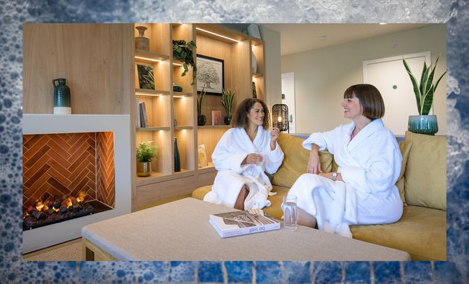 Two women having a chat in robes, sitting on the sofa in the spa area