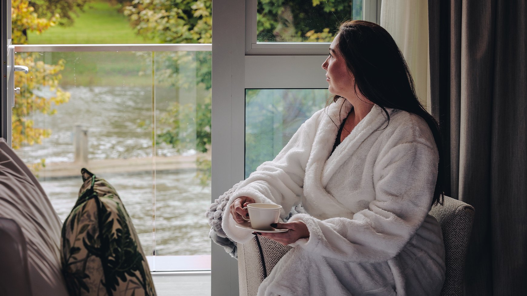 A guest enjoying a cup of tea and the incredible view from her balcony inside a double deluxe room at The Runnymede on Thames