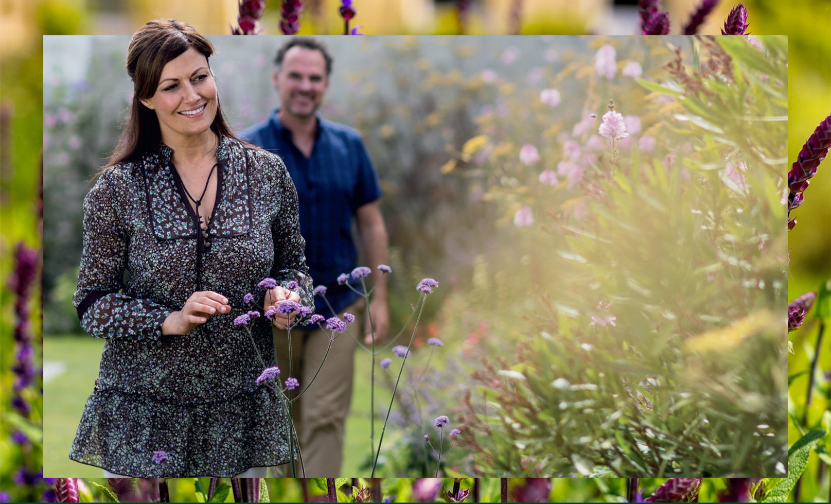 A woman and man stand together in a vibrant garden filled with blooming purple flowers, celebrating Mother's Day at Warner.